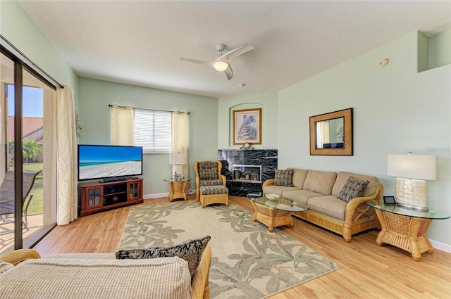 living room featuring a fireplace, baseboards, a ceiling fan, and wood finished floors