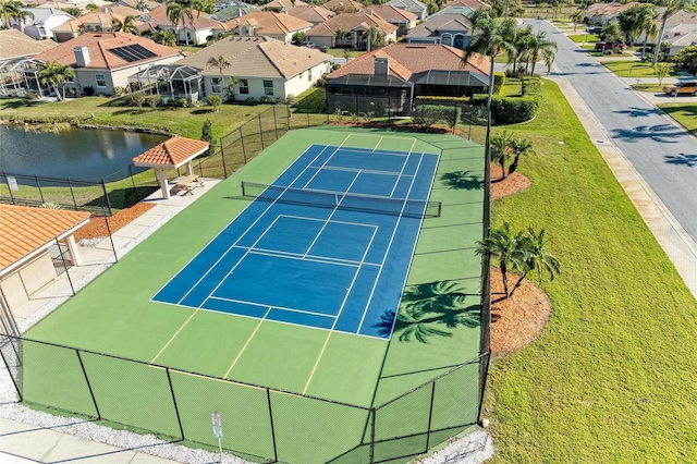 view of tennis court featuring a residential view, a water view, and fence