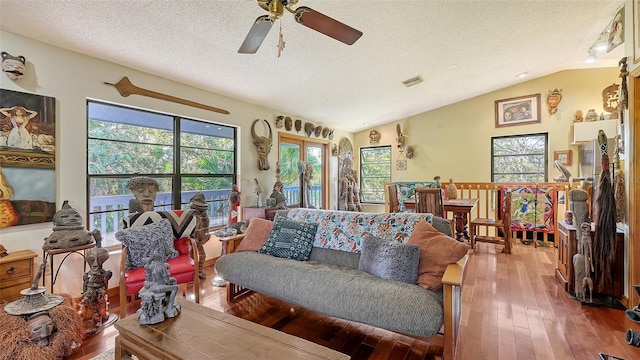 living room featuring visible vents, a ceiling fan, a textured ceiling, hardwood / wood-style floors, and vaulted ceiling