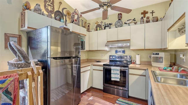 kitchen featuring under cabinet range hood, a sink, wood finished floors, stainless steel appliances, and light countertops