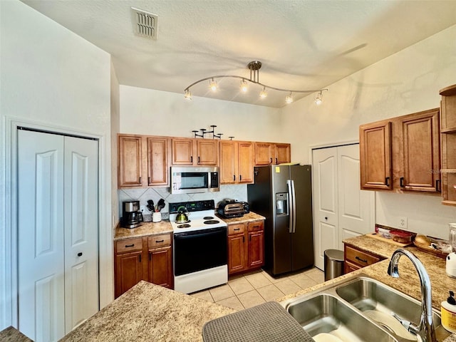 kitchen with visible vents, a sink, appliances with stainless steel finishes, brown cabinetry, and light tile patterned floors