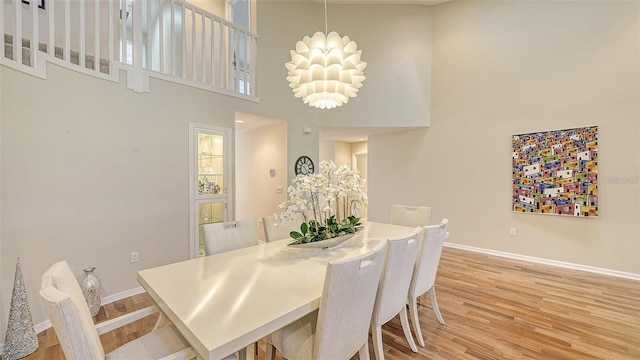 dining area featuring an inviting chandelier, a high ceiling, baseboards, and light wood-type flooring