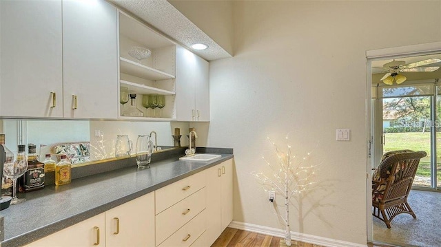 kitchen with wood finished floors, baseboards, open shelves, a sink, and dark countertops