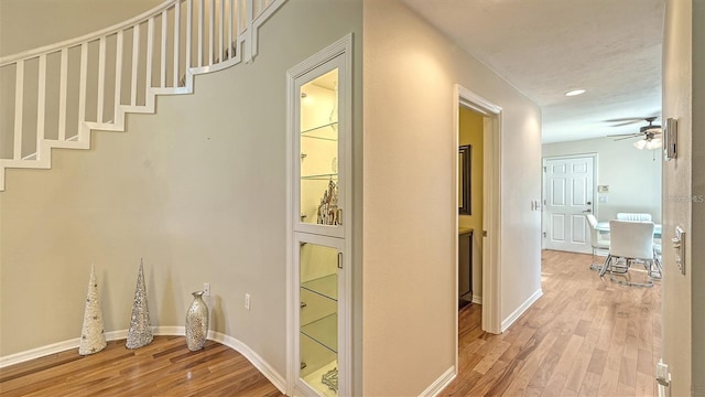 hallway featuring stairs, light wood-style flooring, and baseboards