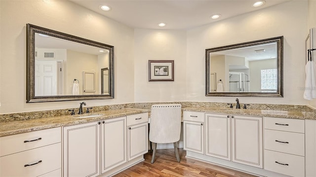 bathroom featuring two vanities, wood finished floors, recessed lighting, and a sink