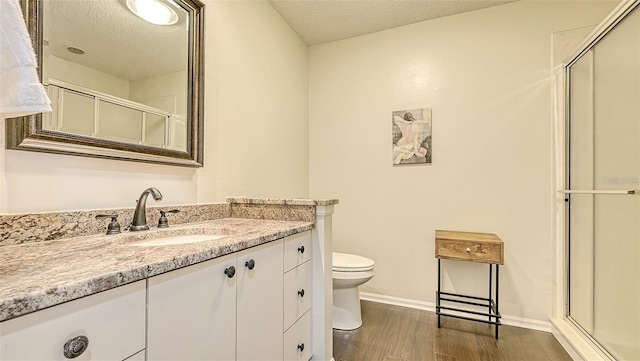 bathroom featuring vanity, wood finished floors, a textured ceiling, toilet, and a shower with door