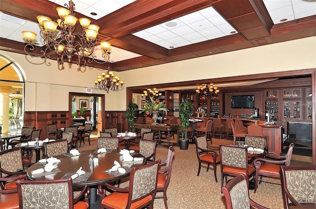 dining area featuring a wainscoted wall, coffered ceiling, carpet floors, an inviting chandelier, and beamed ceiling