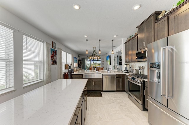 kitchen featuring dark brown cabinetry, light stone counters, a peninsula, stainless steel appliances, and a sink