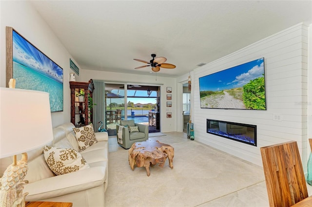 living area with a glass covered fireplace, visible vents, ceiling fan, and carpet flooring