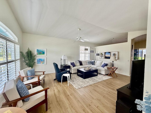 living room featuring lofted ceiling, light wood-style flooring, a ceiling fan, arched walkways, and baseboards