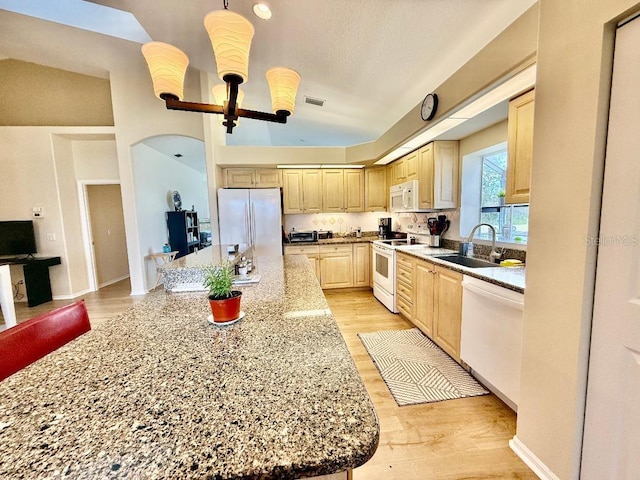 kitchen featuring white appliances, lofted ceiling, light wood-style flooring, light brown cabinetry, and a sink