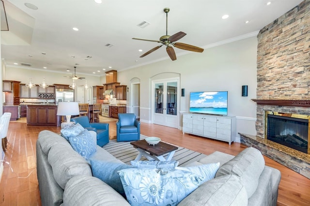 living area featuring visible vents, ornamental molding, light wood-style flooring, a fireplace, and ceiling fan