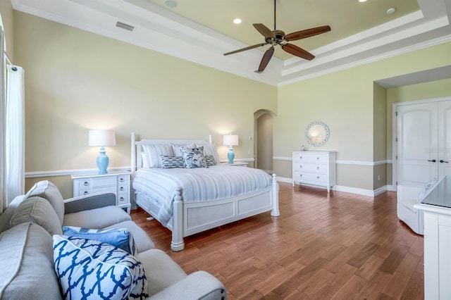 bedroom featuring visible vents, baseboards, a tray ceiling, wood finished floors, and arched walkways