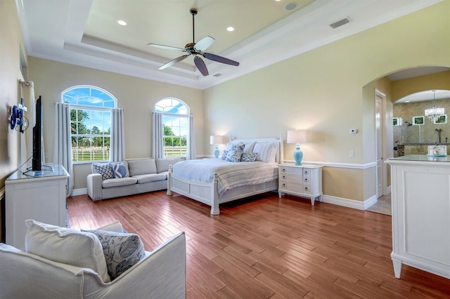 bedroom with visible vents, a tray ceiling, wood finished floors, arched walkways, and baseboards