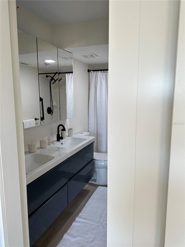 bathroom featuring visible vents, toilet, double vanity, wood finished floors, and a sink