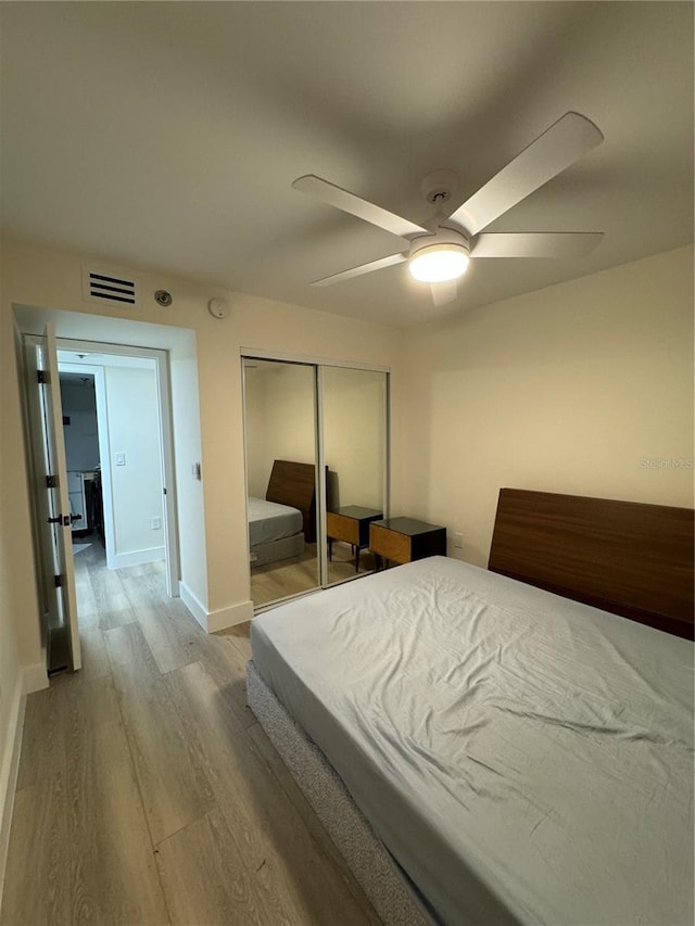 bedroom with a ceiling fan, wood finished floors, visible vents, baseboards, and a closet