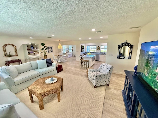 living area featuring recessed lighting, visible vents, light wood finished floors, and a textured ceiling