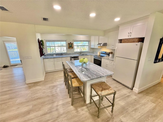 kitchen featuring visible vents, a sink, white cabinets, under cabinet range hood, and appliances with stainless steel finishes