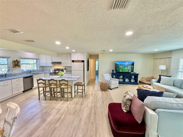 living area featuring visible vents, recessed lighting, a textured ceiling, and light wood-style floors