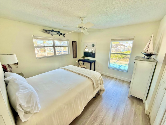 bedroom featuring ceiling fan, baseboards, light wood-type flooring, and a textured ceiling