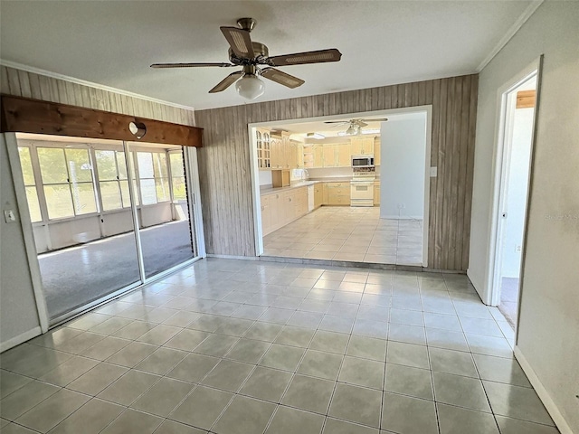 spare room with light tile patterned floors, wooden walls, crown molding, and a ceiling fan