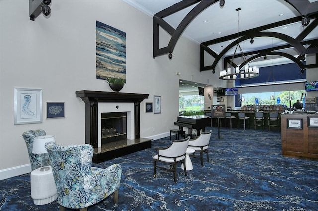 living area featuring a glass covered fireplace, baseboards, a high ceiling, and a chandelier