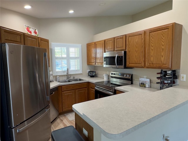 kitchen featuring light countertops, brown cabinets, appliances with stainless steel finishes, a peninsula, and a sink