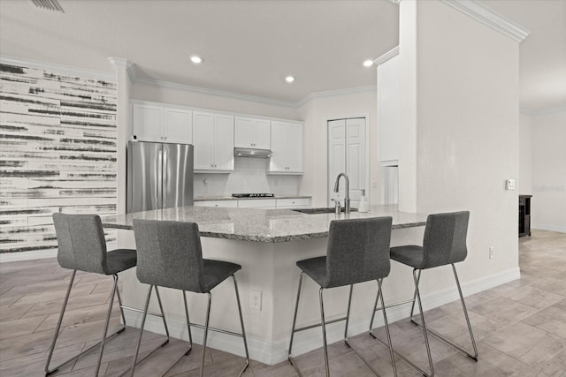 kitchen featuring light stone counters, a breakfast bar, a sink, ornamental molding, and stainless steel refrigerator