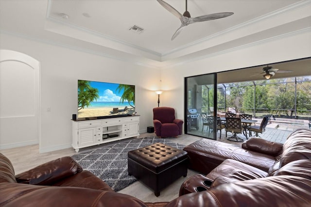 living room with a tray ceiling, plenty of natural light, a ceiling fan, and visible vents