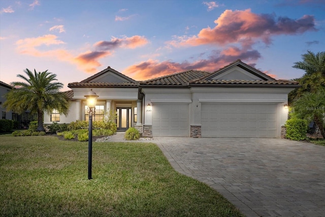 mediterranean / spanish-style home featuring a front yard, stucco siding, a garage, a tile roof, and decorative driveway