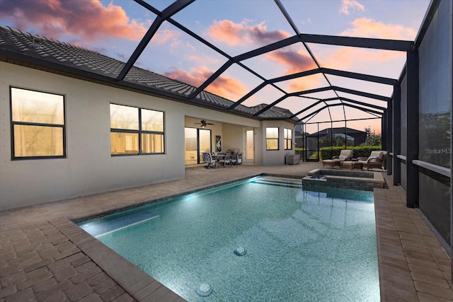 pool at dusk featuring a pool with connected hot tub, a lanai, a ceiling fan, and a patio area