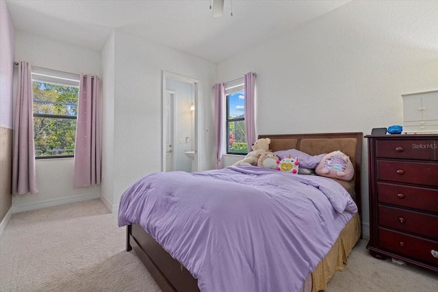 bedroom featuring ensuite bath, light colored carpet, baseboards, and ceiling fan