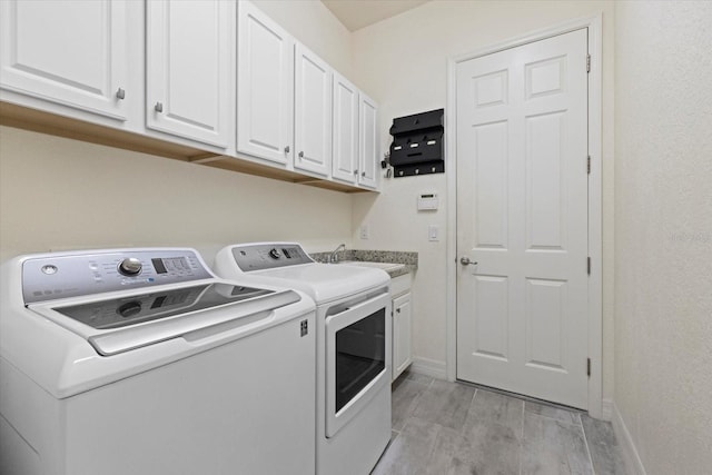 clothes washing area featuring washer and clothes dryer, baseboards, light wood-style floors, and a sink