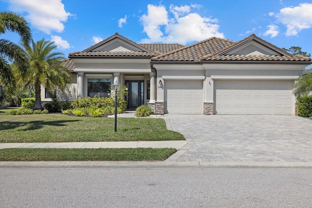 mediterranean / spanish home with a front lawn, a tile roof, stucco siding, decorative driveway, and an attached garage