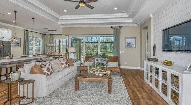 living area with ceiling fan, a raised ceiling, wood finished floors, and ornamental molding