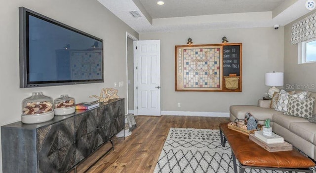 living room featuring visible vents, dark wood-type flooring, a tray ceiling, a textured ceiling, and baseboards