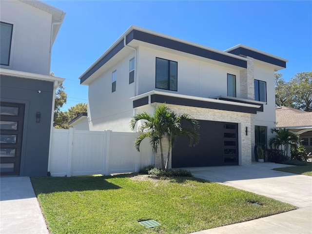 modern home featuring a front yard, fence, driveway, an attached garage, and stucco siding