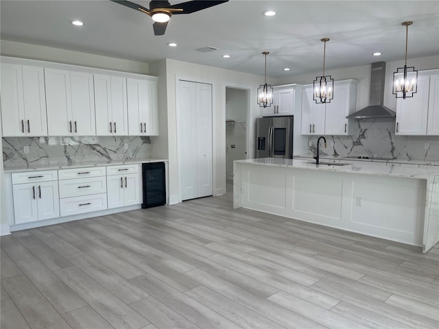 kitchen with visible vents, beverage cooler, stainless steel refrigerator with ice dispenser, white cabinetry, and wall chimney range hood