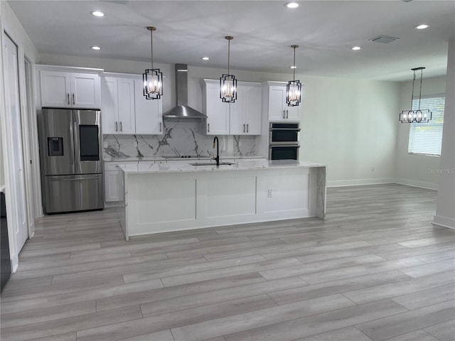 kitchen with a sink, decorative backsplash, appliances with stainless steel finishes, white cabinetry, and wall chimney range hood