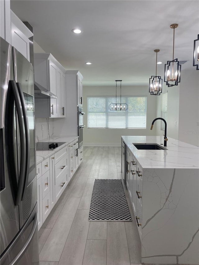 kitchen featuring an island with sink, a sink, white cabinets, appliances with stainless steel finishes, and a chandelier