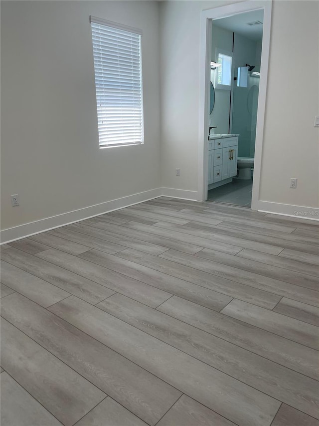 unfurnished bedroom with connected bathroom, baseboards, and light wood-style floors