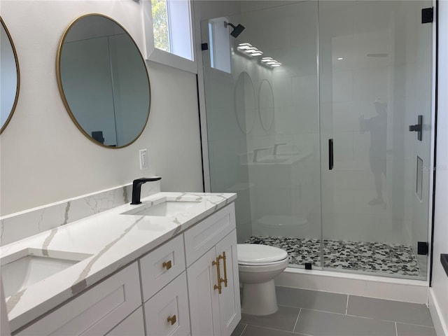 bathroom featuring double vanity, a stall shower, a sink, tile patterned floors, and toilet