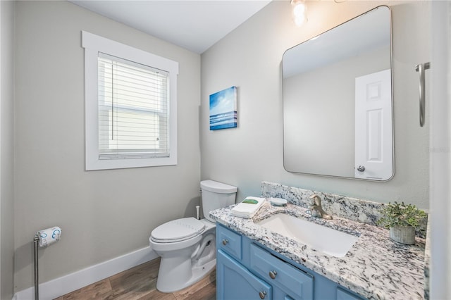 half bath featuring toilet, vanity, wood finished floors, and baseboards