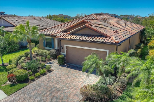 mediterranean / spanish house with stucco siding, an attached garage, a tile roof, and decorative driveway