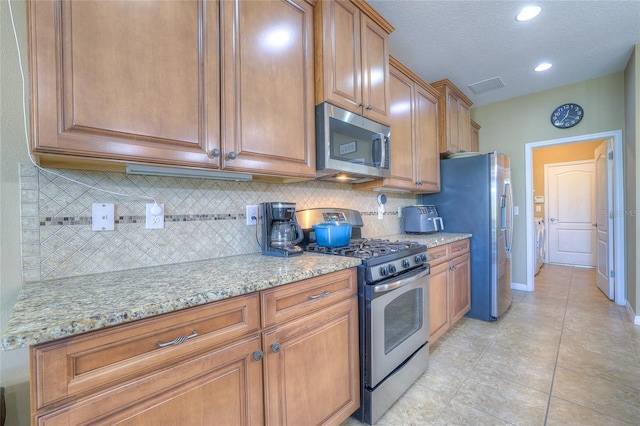 kitchen featuring visible vents, backsplash, light stone counters, appliances with stainless steel finishes, and brown cabinetry