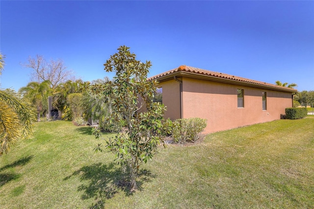 view of side of home with a lawn, a tiled roof, and stucco siding