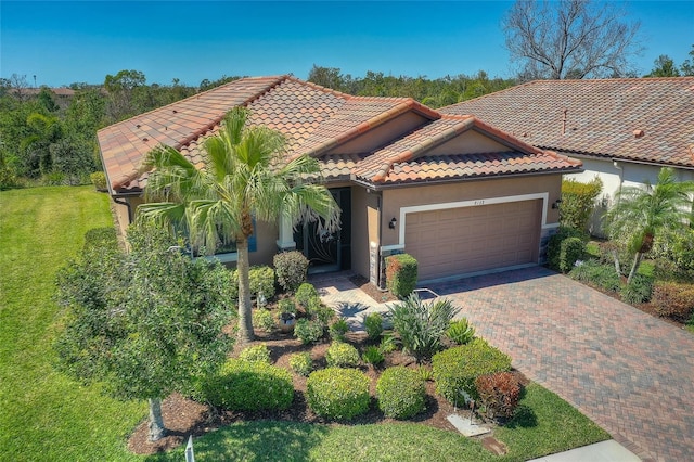 mediterranean / spanish home featuring driveway, stucco siding, a front lawn, a garage, and a tile roof