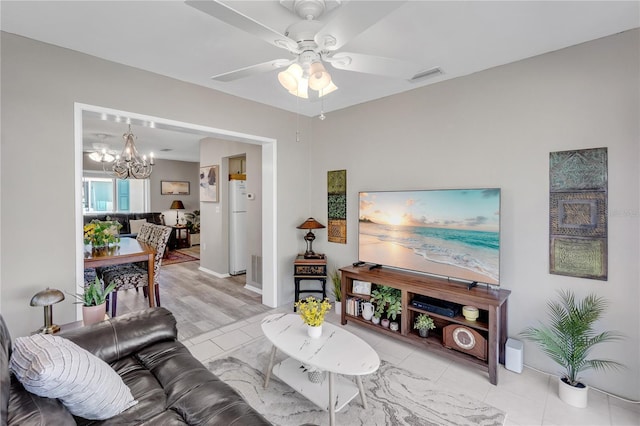 living area featuring light tile patterned floors, visible vents, and ceiling fan with notable chandelier