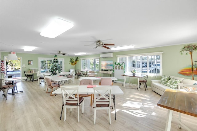 living area with a wall mounted air conditioner, light wood-type flooring, baseboards, and a ceiling fan