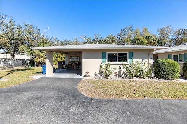 ranch-style home with stucco siding, an attached carport, a front yard, and aphalt driveway